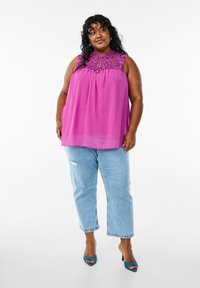 Fuchsian blus med intrikata pärlbroderier vid halslinjen, i kombination med ljusblå, slitna jeans och blå öppna klackskor.