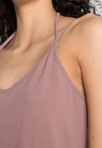Camisole mauve clair en tissu doux avec fines bretelles réglables et coupe décontractée. Présente une texture subtile et un col arrondi.