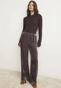Top a maniche lunghe color bordeaux abbinato a pantaloni a palazzo in velluto grigio, con elastico in vita e dettagli di cucitura minimal. Scarpe basse marroni.