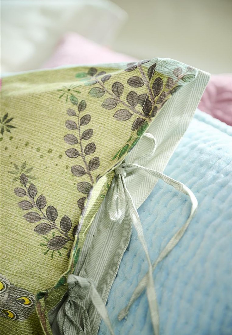 Teksturowana zielona poszewka na poduszkę z wzorem liści, z szaro-białym wykończeniem w jodełkę i wiązaniami, obok niebieskiej pikowanej poduszki.
