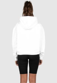 Sweat-shirt blanc avec une grande capuche et une coupe ample, associé à un short noir moulant. Tissu lisse sans motifs ni accessoires visibles.