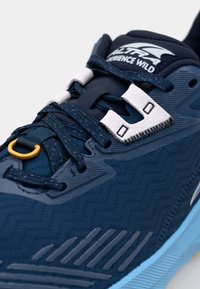 Dunkelblaue Sportschuhe mit strukturiertem Mesh-Obermaterial, kontrastierenden grauen Akzenten und reflektierenden Elementen. Verfügt über Schnürsenkel und eine gelbe Schlaufe.