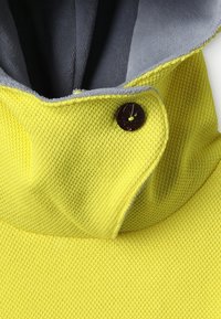 Žlutá texturovaná látka s vysokým límcem, mít šedou podšívku a hnědý knoflíkový akcent. Design je strukturovaný a moderní.