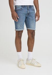 Denim shorts in light blue with rolled cuffs. Features subtle distressing, five pockets, and a classic fit, paired with white sneakers.