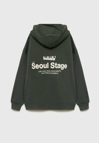 Felpa verde scuro in cotone. Presenta un grande testo grafico bianco sulla schiena che recita "Seoul Stage" con ulteriore testo sottostante.