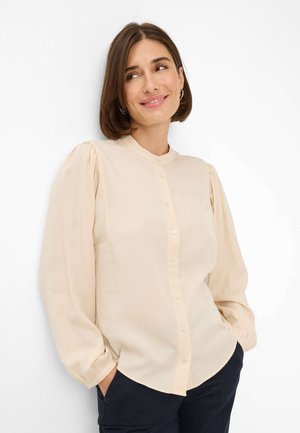 Hellbeige Bluse mit Knopfverschluss und Puffärmeln, glatter Textur und abgerundetem Saum. Verfügt über dezente Knopfdetails an der Vorderseite.