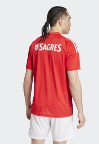 Červený športový dres s bielymi akcentmi a nápisom "SAGRES" vzadu. Vyrobený z priedušného materiálu, s okrúhlym výstrihom a krátkymi rukávmi.