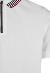 Polo shirt blanc avec un col zippé comportant des rayures bleu marine et rouge. Tissu texturé avec un motif subtil. "HECHTER PARIS" imprimé en blanc.