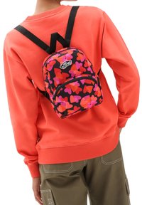 De rugzak heeft een zwarte basis met roze en oranje hartpatronen, aangevuld met zwarte banden en een Vans-logo op het voorvak.