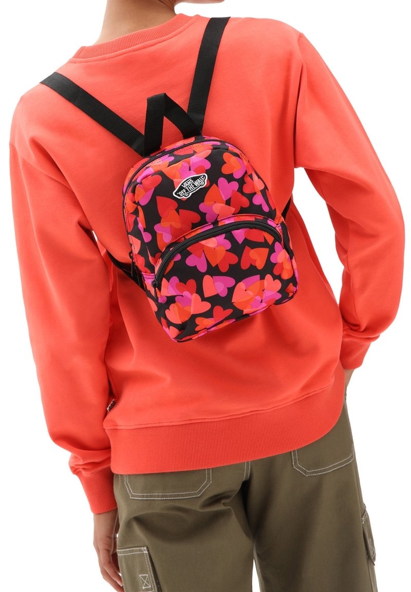 De rugzak heeft een zwarte basis met roze en oranje hartpatronen, aangevuld met zwarte banden en een Vans-logo op het voorvak.