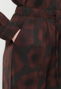 Gros plan sur un pantalon à motifs floraux bordeaux et noirs avec une taille élastique et une main dans la poche latérale.