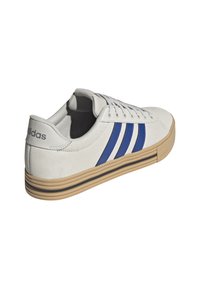 Sneaker bianca in suede con tre strisce blu, suola in gomma naturale e linguetta testurizzata. Presenta un tallone con marchio e una striscia nera a contrasto sulla suola.