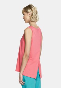 Koralikowy, bezrękawnikowy T-shirt o luźnym kroju, wykonany z bawełny, z detalem wentylacyjnym na plecach i gładką, miękką teksturą.