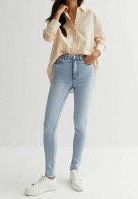 Ljust blå skinny jeans med hög midja, tillverkade av denim. Kombinerat med en ljusbeige knäppskjorta och vita sneakers.