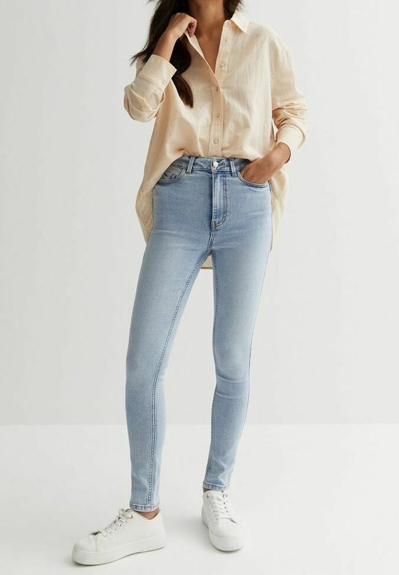 Ljust blå skinny jeans med hög midja, tillverkade av denim. Kombinerat med en ljusbeige knäppskjorta och vita sneakers.