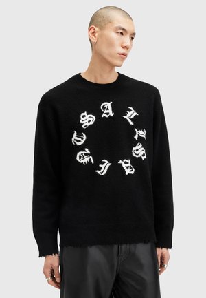 Schwarzer Strickpullover mit einem runden Design und weißem Text, Rundhalsausschnitt und fransigem Saum. Das Material wirkt weich mit einer strukturierten Oberfläche.