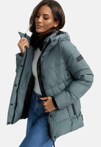 Hooded puffer jacket in muted teal, featuring a zip and snap closure, adjustable drawstrings, and black accents. Soft, quilted texture.