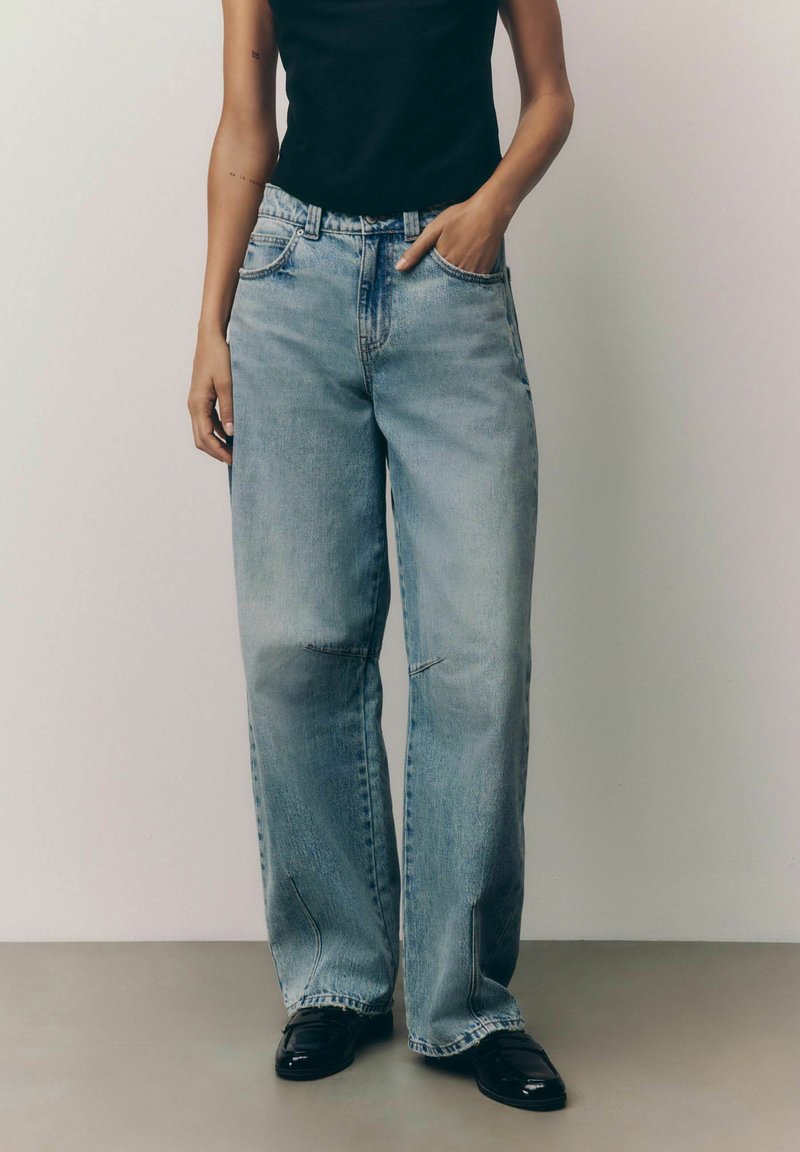 Ljust blå denim byxor med vida ben och en urtvättad finish, framfickor och en avslappnad passform. Kombinerat med en svart åtsittande linne och mörka skor.