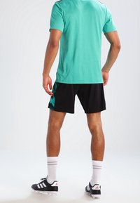 Turkusowa koszulka sportowa z czarnymi szortami w odcieniach teal. Czarne buty i białe skarpety do kolan z szarymi paskami.