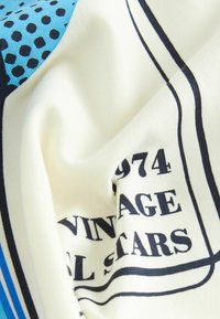 Katoenen stof met een crème basis, voorzien van een blauwe en zwarte print, inclusief stippen en tekst die zegt "1974 VINTAGE ALL STARS." Zachte textuur.