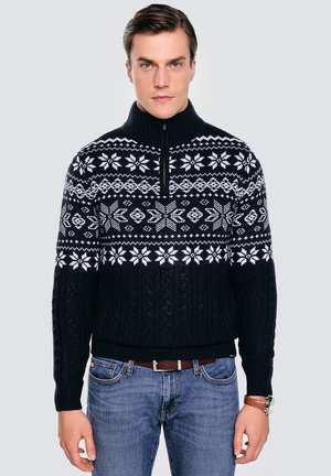 Granatowy sweter z dzianiny z wysokim kołnierzem, ozdobiony białymi geometrycznymi wzorami i śnieżynkami. Rybkowane mankiety i dół, zamek błyskawiczny przy szyi.