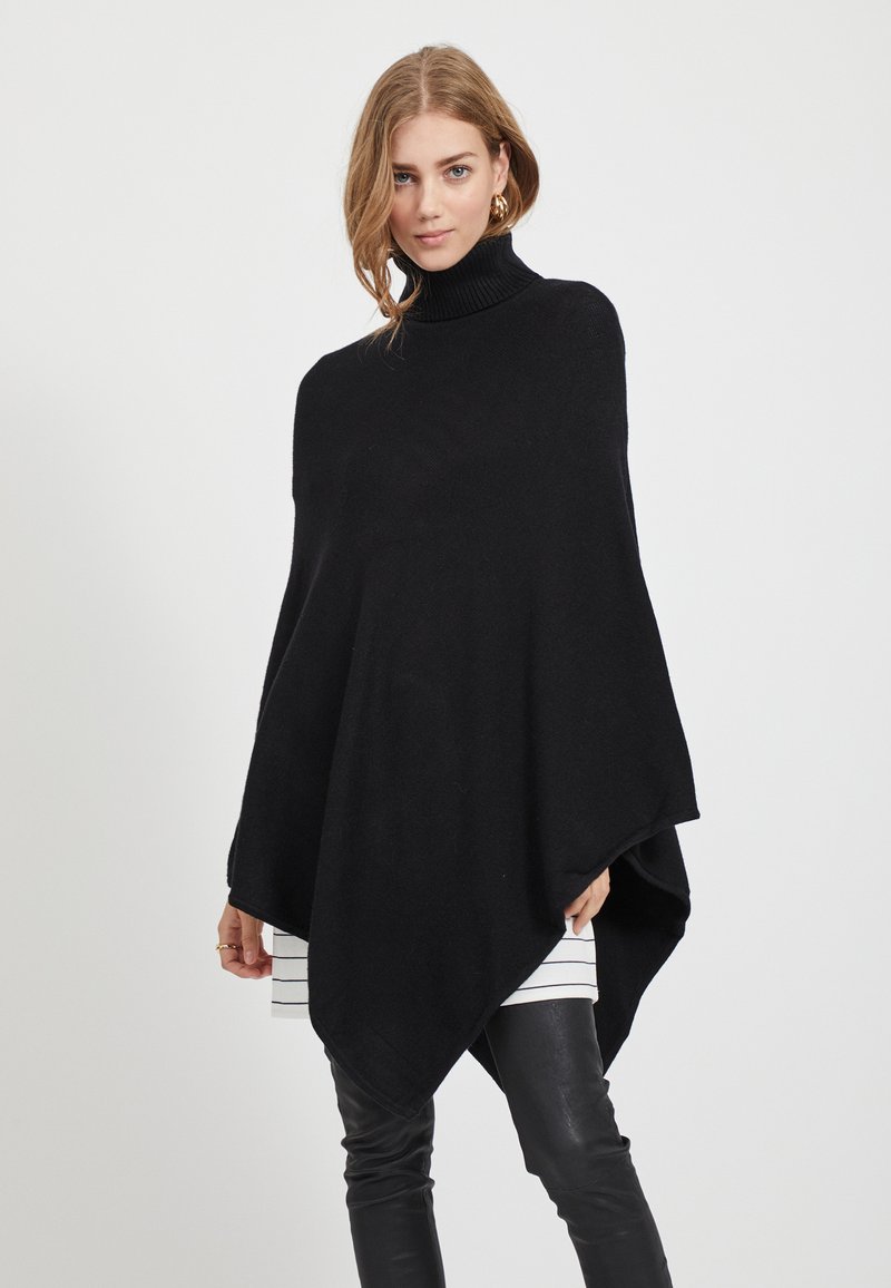 Poncho preto de gola alta, feito de um tecido knit suave, com uma silhueta drapeada, bainha pontiaguda e aberturas largas para os braços.