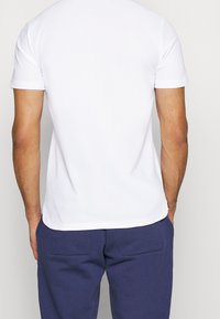 Bílý tričko s krátkým rukávem a hladkým povrchem, s oblečeným zakřiveným lemem, doplněné tmavě modrými kalhotami s dvěma zadními kapsami.