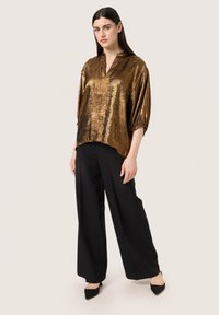 Blusa metallica dorata con una vestibilità morbida, maniche a 3/4 e colletto alla cinese, abbinata a pantaloni neri a gamba larga e tacchi a punta.