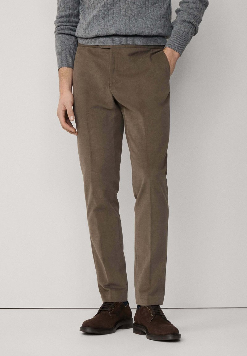 Brązowe spodnie wizytowe z gładkiego materiału, o dopasowanym kroju, z bocznymi kieszeniami, w zestawie z ciemnobrązowymi butami na sznurówki.