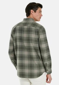 Camicia di flanella a quadri verdi con una vestibilità comoda, maniche lunghe e polsini con bottoni. Presenta un orlo arrotondato e sottili accenti grigi.