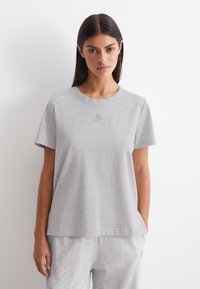 Grijze katoenen t-shirt met korte mouwen, een ronde hals en een subtiele reliëflogo op de borst. Zachte textuur en een comfortabele pasvorm.