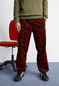 Röda snabba sammetsbyxor med ett blommönster, tillsammans med en grön sweatshirt och svarta skor med vita ränder.