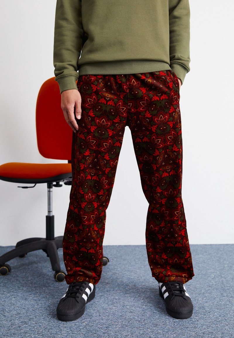 Röda snabba sammetsbyxor med ett blommönster, tillsammans med en grön sweatshirt och svarta skor med vita ränder.