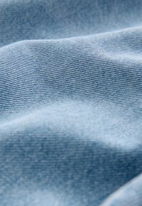 Világoskék farmeranyag sima textúrával, amely finom halszálkás mintázatot és lágyan hullámzó redőket mutat.