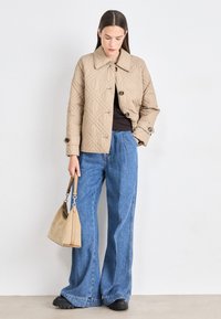 Beige quilted jacket with large collar and button closure, paired with wide-leg blue jeans and a tan shoulder bag. Black platform shoes.