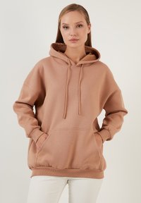 Rozpinana bluza z kapturem w miękkim beżowym materiale o luźnym kroju, z kieszenią kangurką, ściągaczami przy mankietach i u dołu oraz sznurkami przy szyi.