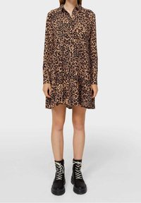 Sukienka w panterkę z długim rękawem w odcieniach brązu i czerni, z kołnierzykiem i warstwowym dołem, zestawiona z czarnymi sznurowanymi botkami.