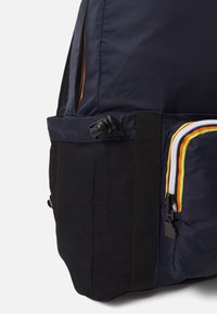 Zaino navy con una tasca laterale in rete nera testurizzata, dotato di una cerniera multicolore e di una cintura di chiusura per una chiusura sicura.