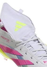 Bottes de football blanches avec une surface texturée, des touches de rose vif et de bleu, et un design montants. Logo jaune remarquable sur le col.