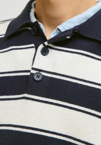 Námořnická a smetanová pruhovaná polo košile se dvěma černými knoflíky, z bavlněného materiálu, s límečkem a texturou na látce.