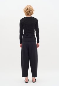 Fekete, hosszú ujjú felső, texturált felülettel, laza fekete nadrággal párosítva. A modell hátulról látható, lapos fekete szandált visel.