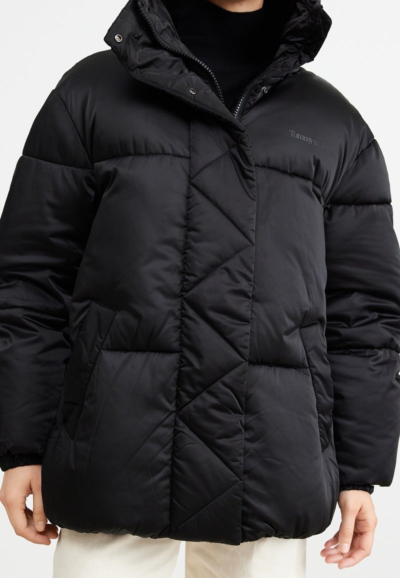 Svart puffjacka med huva, med en quiltad design, blixtlås och två sidofickor. Tillverkad av ett mjukt, glänsande material.