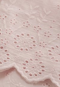 Rosa tyg med intrikata blommönster broderade, med utskurna mönster och vågiga kanter, tillverkat av lättviktsbomull.