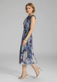 Vestido de acuarela azul con un corsé ajustado, falda voletada y diseño sin mangas. Combinado con sandalias plateadas de tiras.