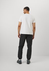 Weißes Baumwoll-T-Shirt mit kurzen Ärmeln, kombiniert mit schwarzen Hosen mit elastischem Bund. Die Schuhwerk zeigt eine Mischung aus Blau- und Grautönen.