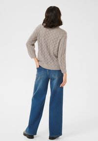 Maglione grigio chiaro a maglia con motivo a rombi, maniche 3/4, abbinato a jeans a gamba larga blu a vita alta e stivaletti neri.