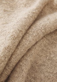 Tissu beige texturé avec une surface douce et duveteuse. Le matériau semble chaud, avec un tissage légèrement irrégulier et des variations de couleur subtiles.