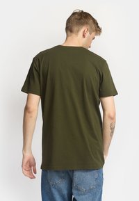 Camiseta de algodón color verde oliva con mangas cortas, escote redondo y un ajuste relajado, mostrada desde atrás contra un fondo blanco liso.