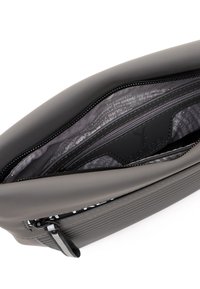 Pochette grigia con zip e righe orizzontali, aperta per mostrare la tasca interna nera e la fodera in tessuto stampato con dettagli del logo del marchio.