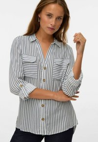 Chemise à rayures en tissu léger, dotée de deux poches poitrine, de manches roulées et de boutons contrastants. La palette de couleurs est blanche et marine.